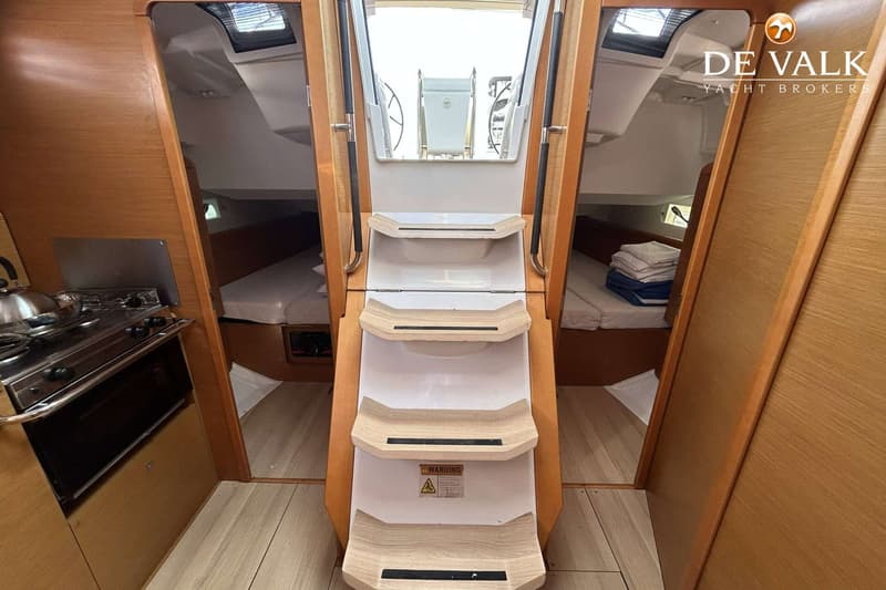 De foto toont een interieur van een boot met een trap naar het dek, een kombuis en twee slaapcabines.