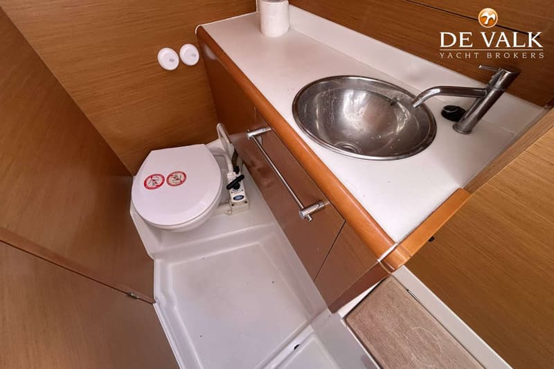 Een interieurfoto toont een toilet en een wastafel met kraan, ingebouwd in een houten meubel met een wit aanrechtblad.