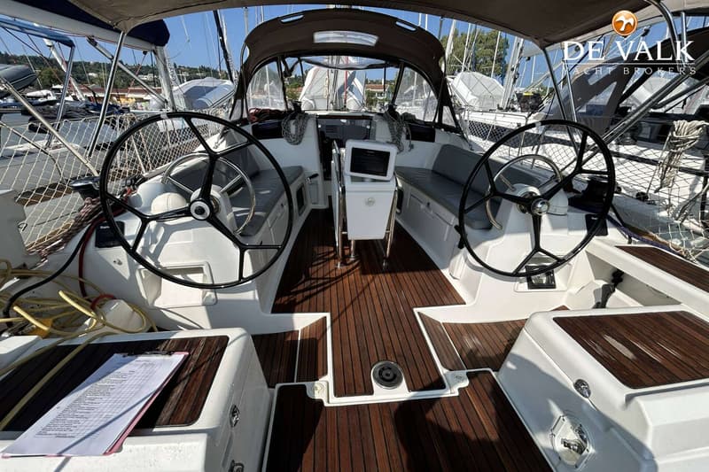 De foto toont de cockpit van een zeilboot met twee stuurwielen, een houten vloer en een navigatiescherm.