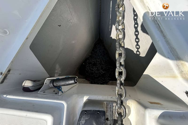 Een ankerketting ligt opgerold in de ankerbak van een boot, met een deel van de ketting omhoog hangend.