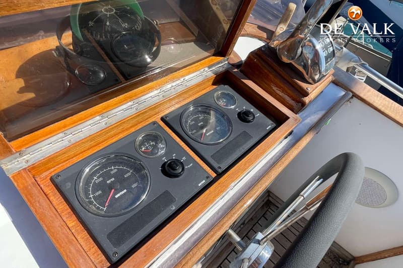 Een detailfoto van het dashboard van een boot met twee toerentellers, een kompas en een stuurwiel.