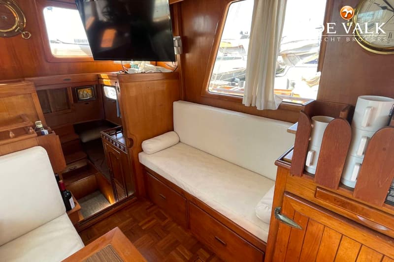 De foto toont een houten interieur van een boot met een bank, een televisie en een raam met gordijnen.