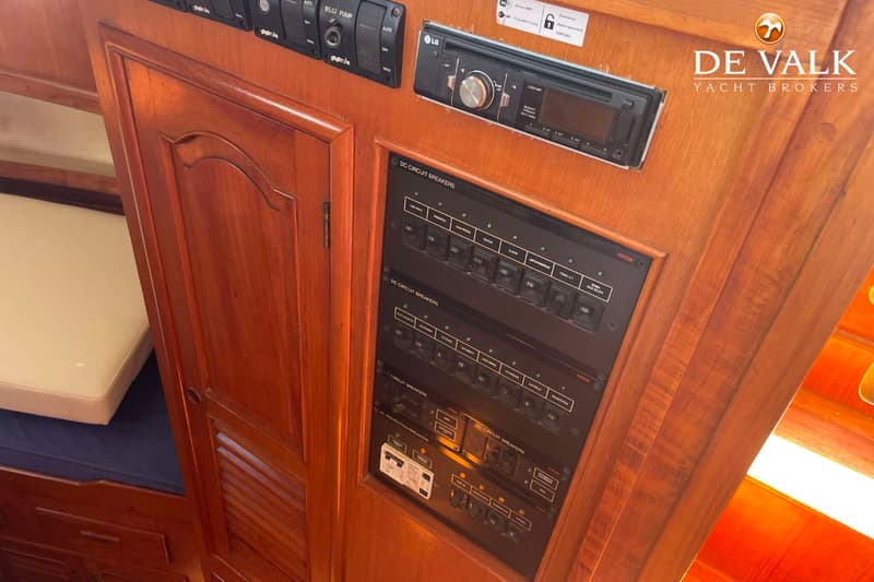 Een houten interieur met een LG radio, een bedieningspaneel met schakelaars en een bed met blauw en wit matras.