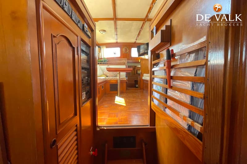 Een interieur van een boot met houten lambrisering, een houten vloer, een zithoek en een paneel met schakelaars.