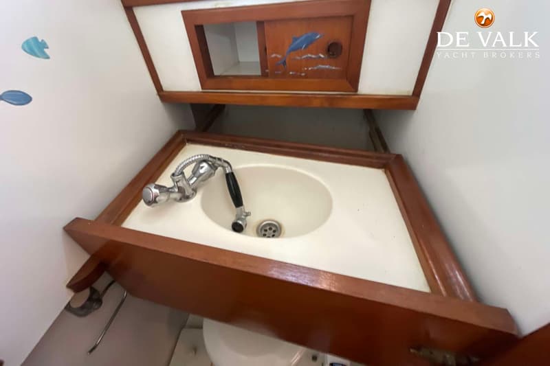 Een witte wasbak met een chromen kraan en een houten rand, daarboven een houten kastje met een dolfijn erop.