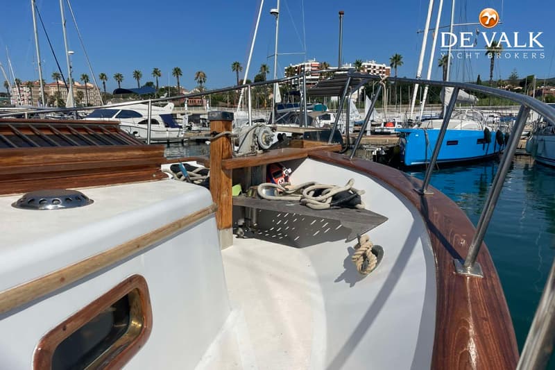 Een vooraanzicht van een boot met een ankerlier, touwen en een houten reling, liggend in een haven.