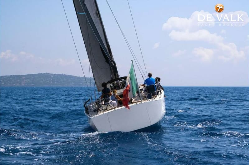 Een witte zeilboot met een zwart zeil vaart op open water met een Italiaanse vlag aan de achtersteven. — Baltic 60