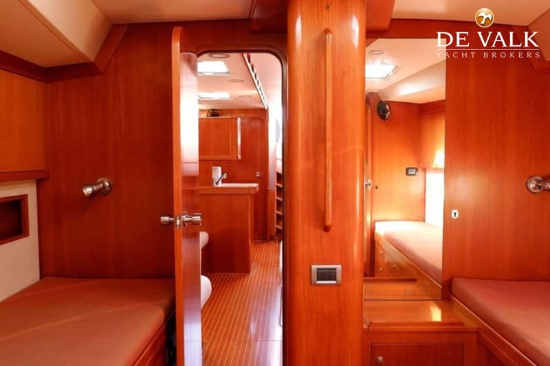 De foto toont een interieur van een boot met houten wanden en vloer, twee bedden met oranje matrassen en een open deur naar…