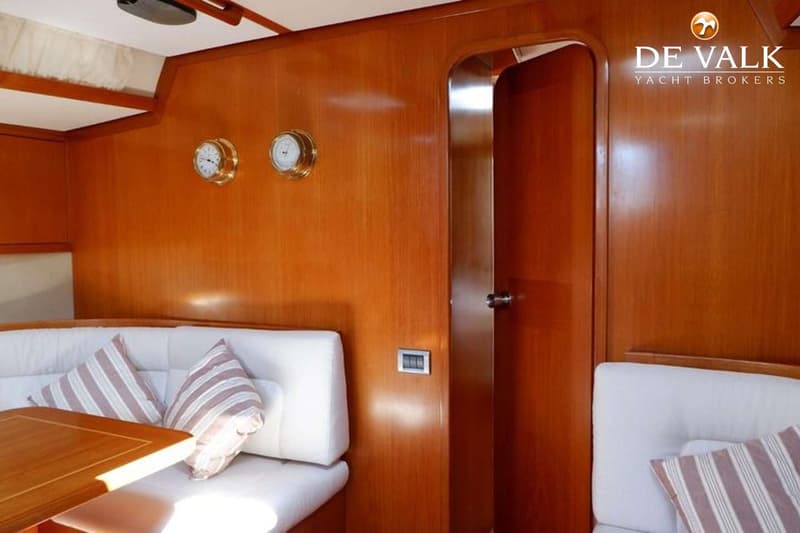 Een interieur van een boot met houten wanden, witte banken, een houten tafel, twee klokken en een open deur. — Baltic 60