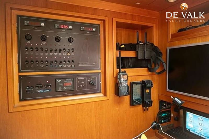 Een houten interieur met een bedieningspaneel, twee portofoons, een monitor en een laptop.