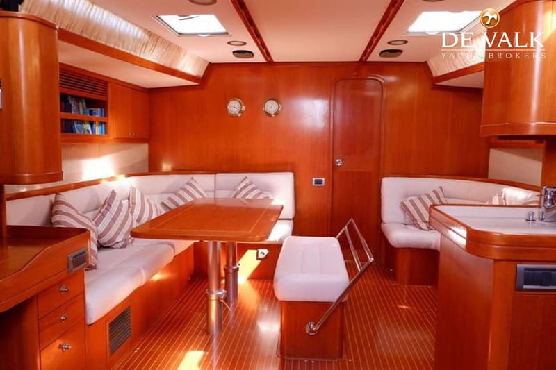 Een interieur van een boot met houten wanden en vloer, witte banken met gestreepte kussens, een houten tafel en een aanrecht.