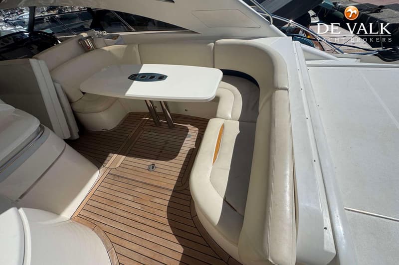 Een bootinterieur met een U-vormige witte bank, een witte tafel en een houten vloer.