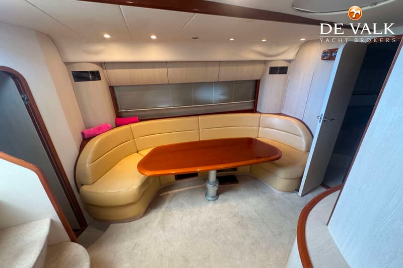 Een interieur van een boot met een U-vormige beige bank, een houten tafel en een tapijt op de vloer. — Princess V48