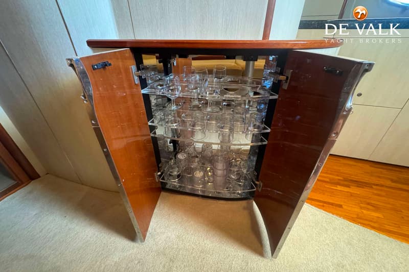 Een open barkast met glazen, geflankeerd door twee houten deuren met metalen randen, staat op een licht tapijt.