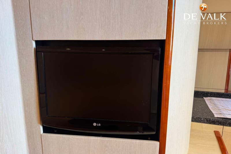 Een zwarte LG televisie is ingebouwd in een lichtgekleurde houten wand, met een donker aanrechtblad rechts.
