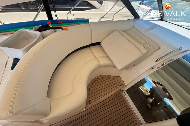Een crème U-vormige bank met kussens en een houten vloer op een boot. — Princess V48