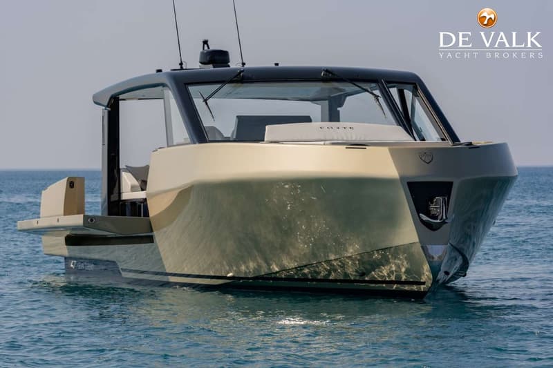 Een moderne motorboot met een goudkleurige romp en zwarte opbouw ligt in rustig, blauw water onder een heldere hemel.