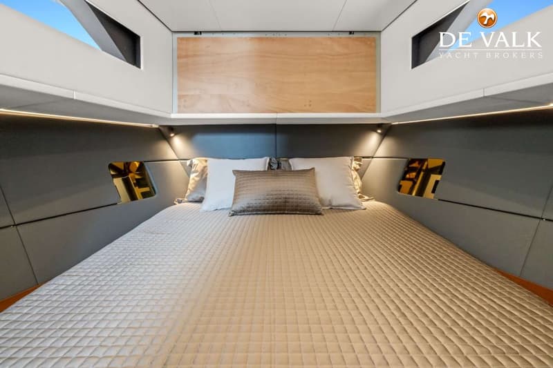 Een kajuit met een tweepersoonsbed, vier kussens, en een gewatteerde sprei, met ingebouwde verlichting en ramen.