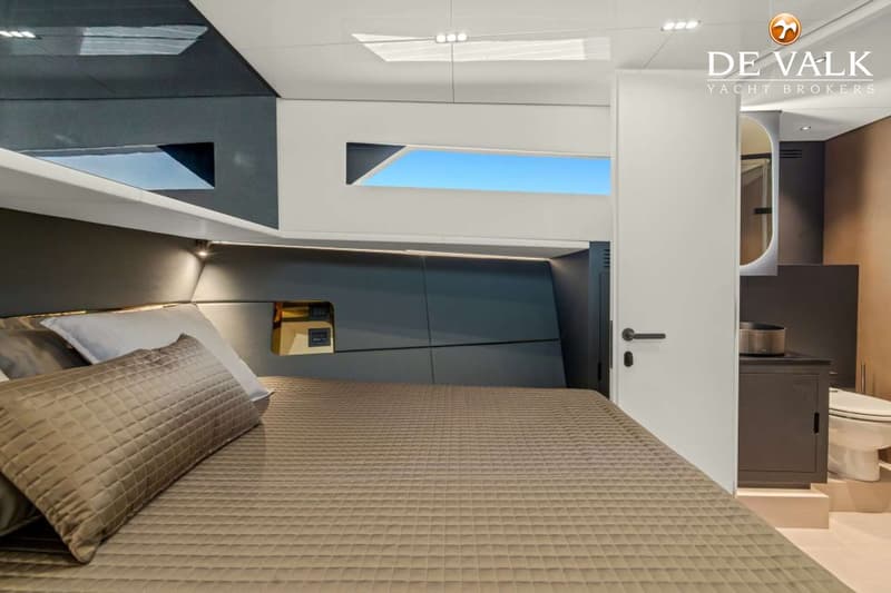 Een slaapkamer in een boot met een groot bed, kussens, een raam met blauwe lucht en een badkamerdeur. — Forte 47 GT