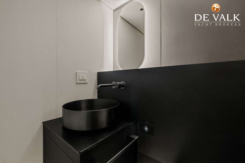 Een moderne badkamer met een zwarte wastafel en kraan, een verlichte spiegel en een donker aanrechtblad.