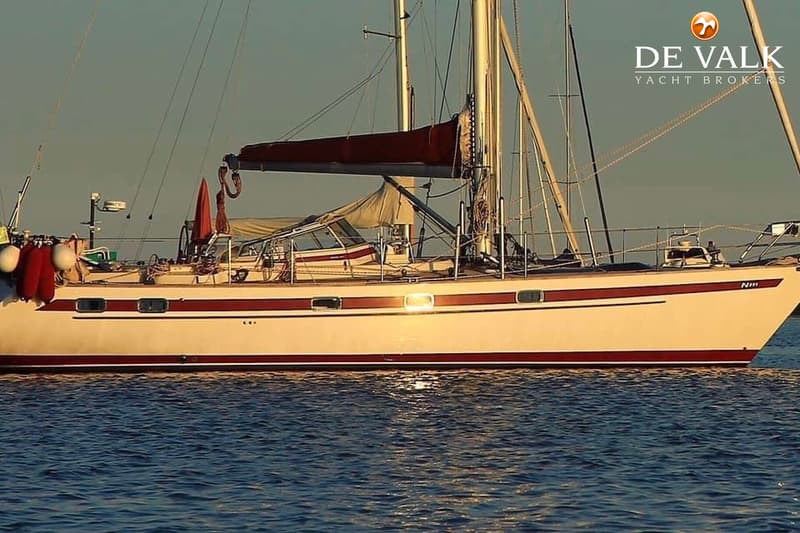 Een witte zeilboot met rode strepen op de romp drijft op blauw water onder een heldere hemel. — Najad 391