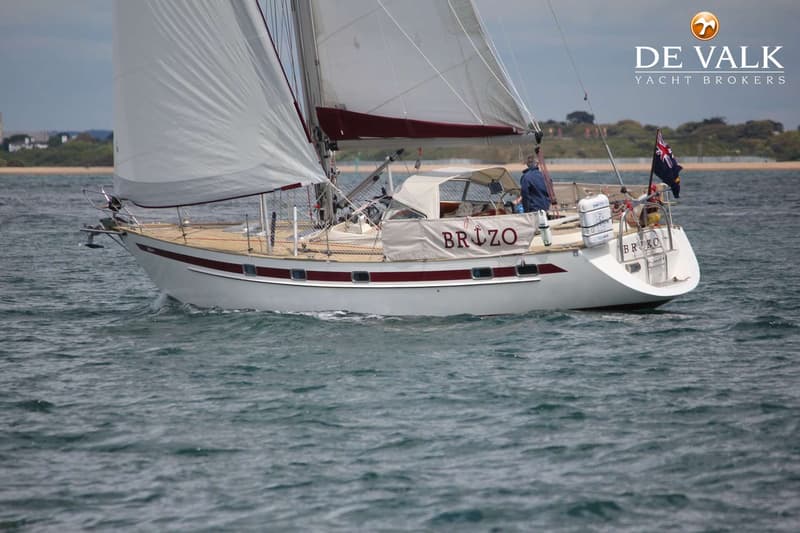 Een witte zeilboot met rode strepen en de naam "BRIZO" op de zijkant vaart op het water. — Najad 391