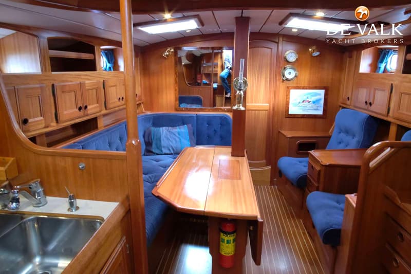 Een interieur van een boot met houten wanden, blauwe kussens, een tafel en een gootsteen. — Najad 391