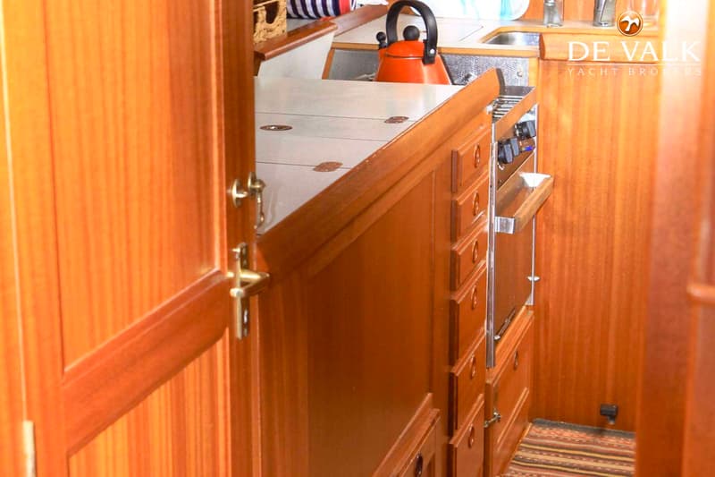 Een houten interieur met een kombuis, inclusief een fornuis, gootsteen en een oranje fluitketel.