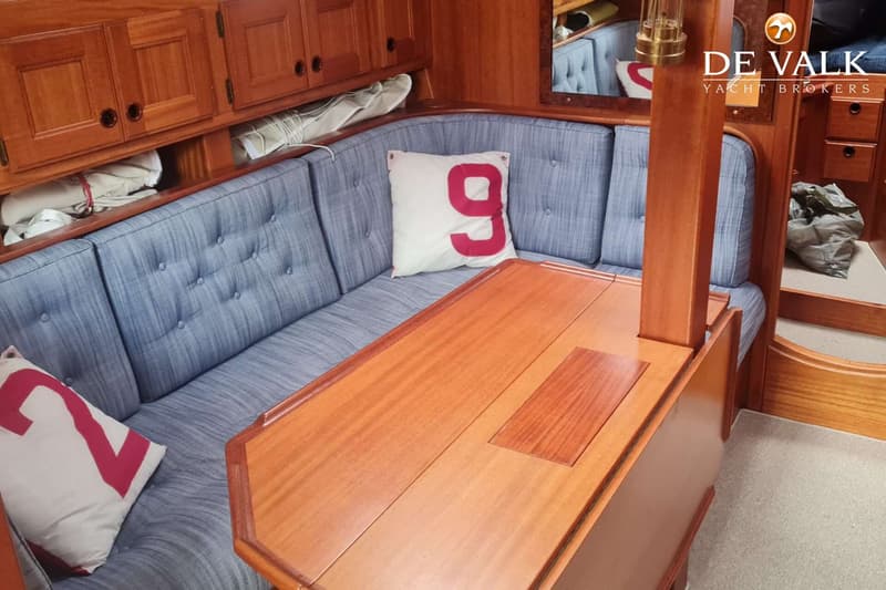 Een interieur van een boot met houten kasten, een blauwe bank met kussens en een houten tafel. — Najad 391