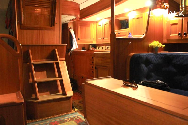 Een interieur van een boot met houten lambrisering, een trapje, een donkerblauwe bank en een tafel. — Najad 391