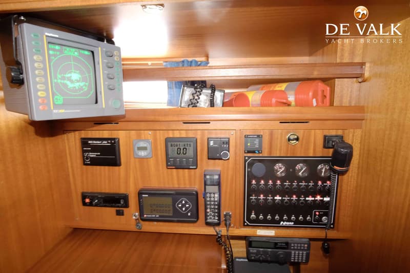 Een houten interieur met diverse navigatie-instrumenten, meters en schakelaars, waaronder een radar en een marifoon.