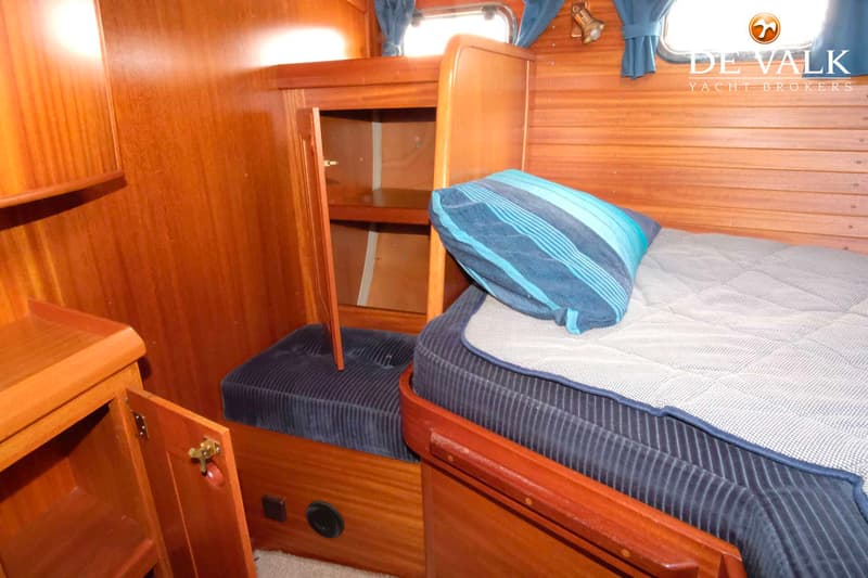 Een kajuit met houten wanden, een bed met blauw kussen en een open kastje met planken. — Najad 391