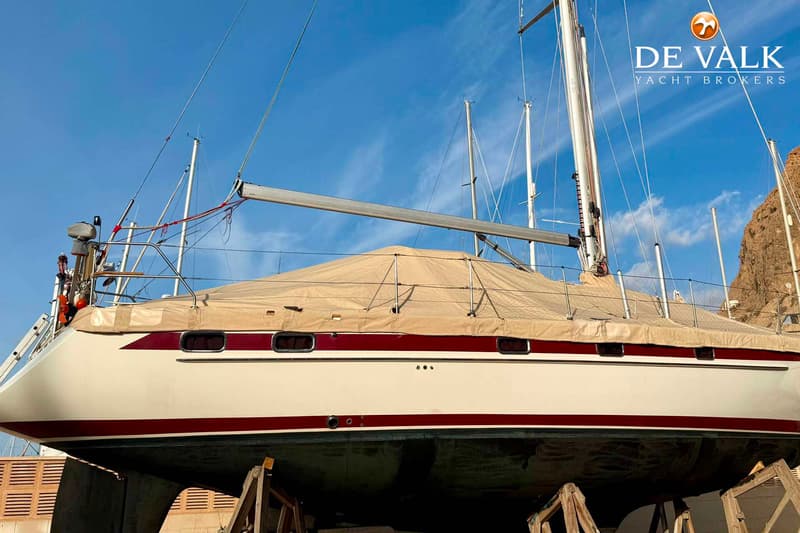 Een zeilboot met een witte romp en rode strepen staat op bokken, gedeeltelijk bedekt met een beige zeil. — Najad 391