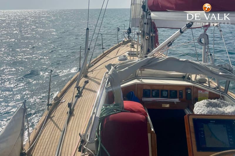 Een zeilboot vaart op open water, met een houten dek, een rood zeil en een grijze buiskap. — Najad 391