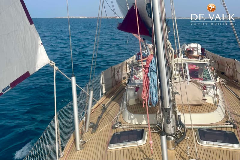 Een zeilboot met houten dek vaart op open water met een kustlijn zichtbaar in de verte. — Najad 391