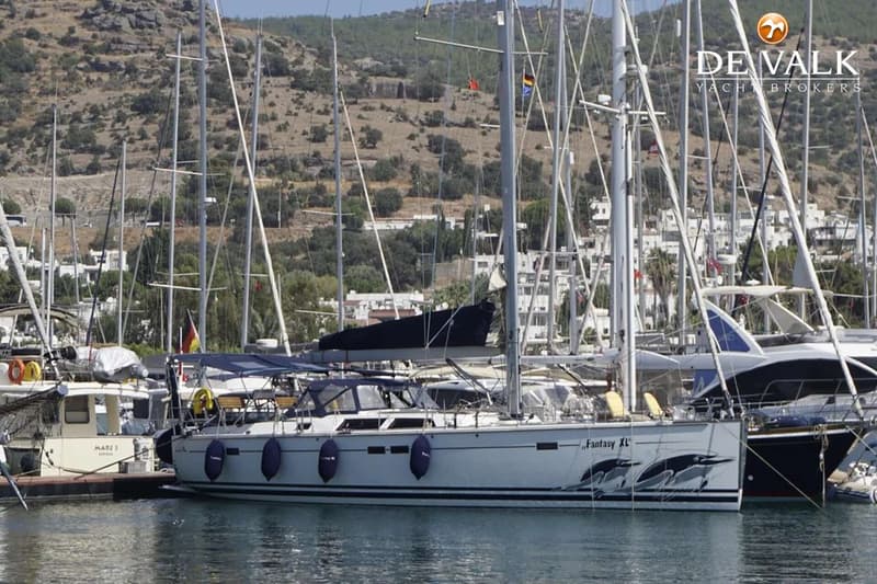 Een witte zeilboot met de naam "Fantasy XL" en dolfijn-afbeeldingen op de romp ligt aangemeerd in een haven. — Hanse 540e