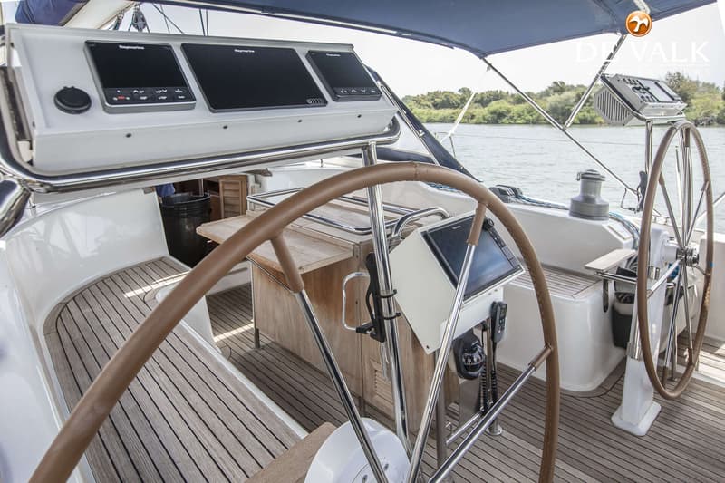 De foto toont het dek van een zeilboot met twee stuurwielen, navigatie-instrumenten en een houten vloer. — Hanse 540e