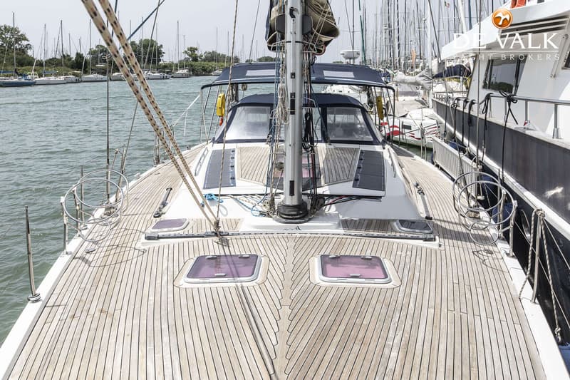 Een zeilboot met een houten dek en twee luiken, afgemeerd in een haven met andere boten. — Hanse 540e