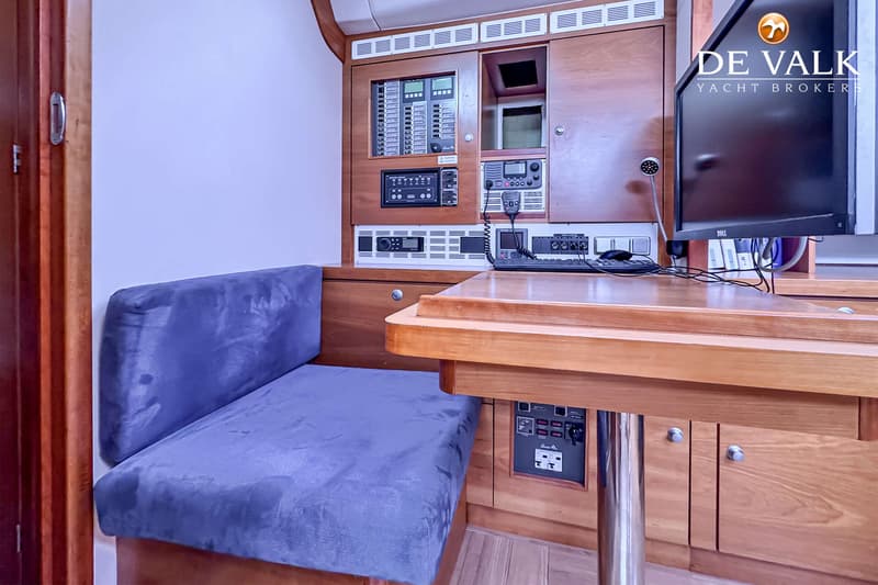 Een interieur van een boot met een houten tafel, een blauwe bank, een monitor en diverse bedieningspanelen. — Hanse 540e