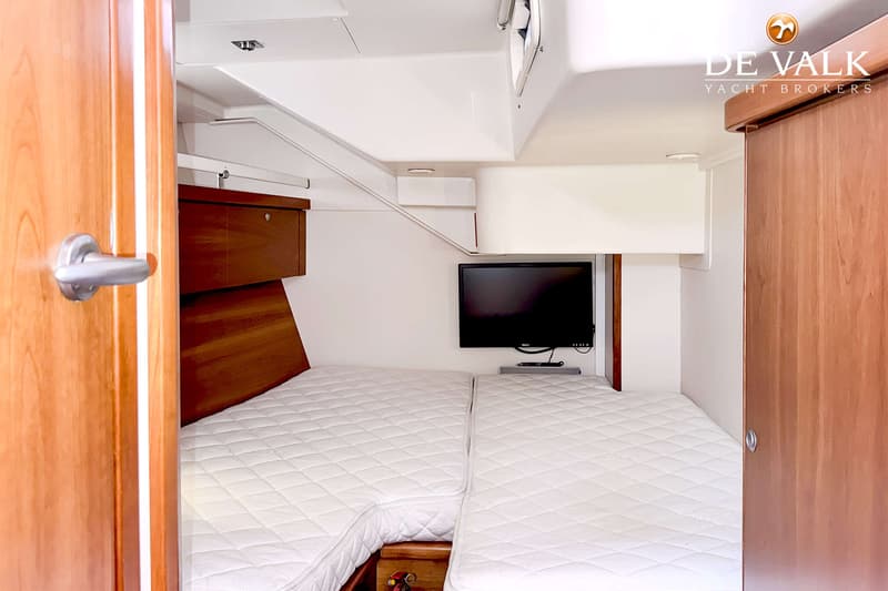 Een kajuit met twee bedden met witte matrassen, een tv aan de muur en houten kasten en deuren. — Hanse 540e