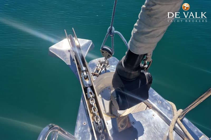 De foto toont het voordek van een boot met een ankerketting, een rolfok en een ankerlier, boven helder turquoise water.
