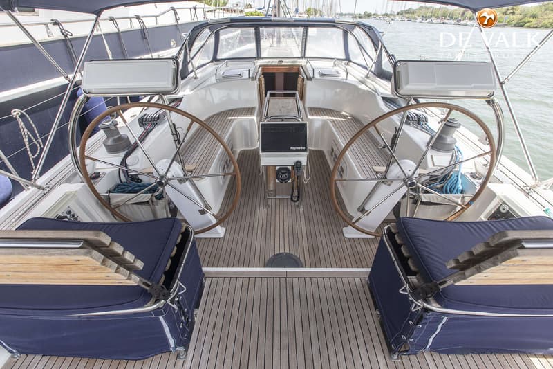 De foto toont de kuip van een zeilboot met twee stuurwielen, een houten dek en blauwe kussens. — Hanse 540e