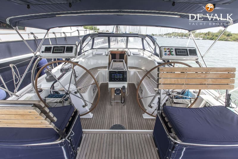 De cockpit van een zeiljacht met twee stuurwielen, een teakhouten dek en blauwe kussens.