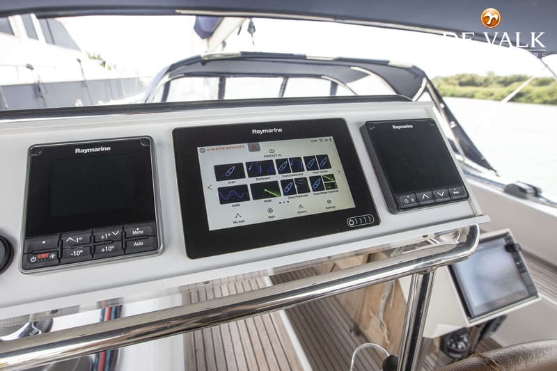 Drie Raymarine schermen zijn zichtbaar op het dashboard van een boot, met een houten dek op de achtergrond. — Hanse 540e