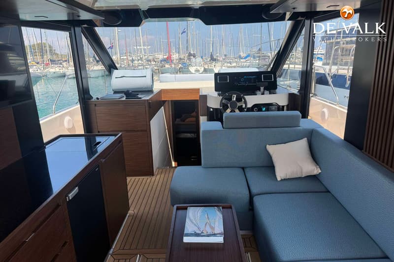 De foto toont het interieur van een boot met een blauwe bank, een stuurwiel en uitzicht op een haven vol boten. — Wia 520 HT