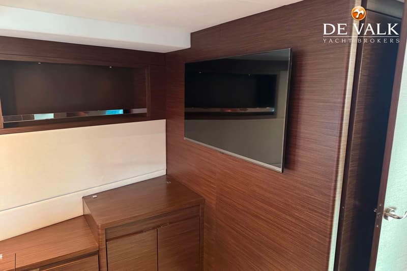 Een interieur met een flatscreen-tv aan de wand, een wit gestoffeerde bank en houten kasten en wandbekleding.