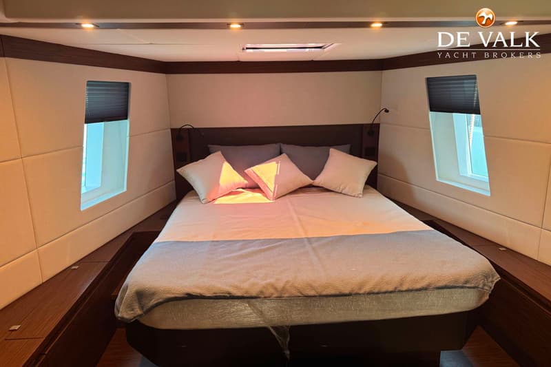 Een slaapkamer met een tweepersoonsbed, twee ramen met jaloezieën, en een dakraam, met het logo "DE VALK YACHT BROKERS".