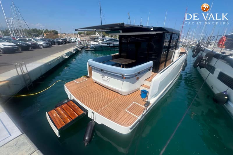Een witte motorboot met een houten dek en een uitschuifbaar zwemplateau ligt aangemeerd in een haven. — Wia 520 HT