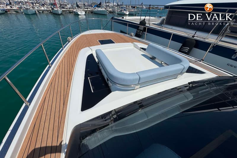 De foto toont het voordek van een boot met een teakhouten dek, een zonnebed met lichtblauwe kussens en een rvs-reling.