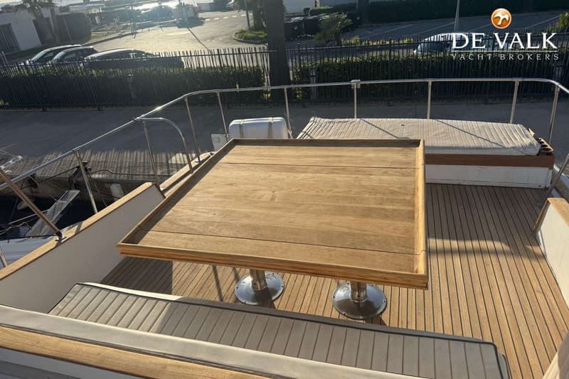 Een houten tafel met twee zilverkleurige poten staat op een houten dek met banken en een reling.